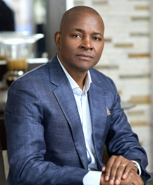 Pastor Roy Bondo speaking passionately at a podium during a church service, wearing formal attire. Natural light streams through stained glass windows in the background, creating an inspiring atmosphere